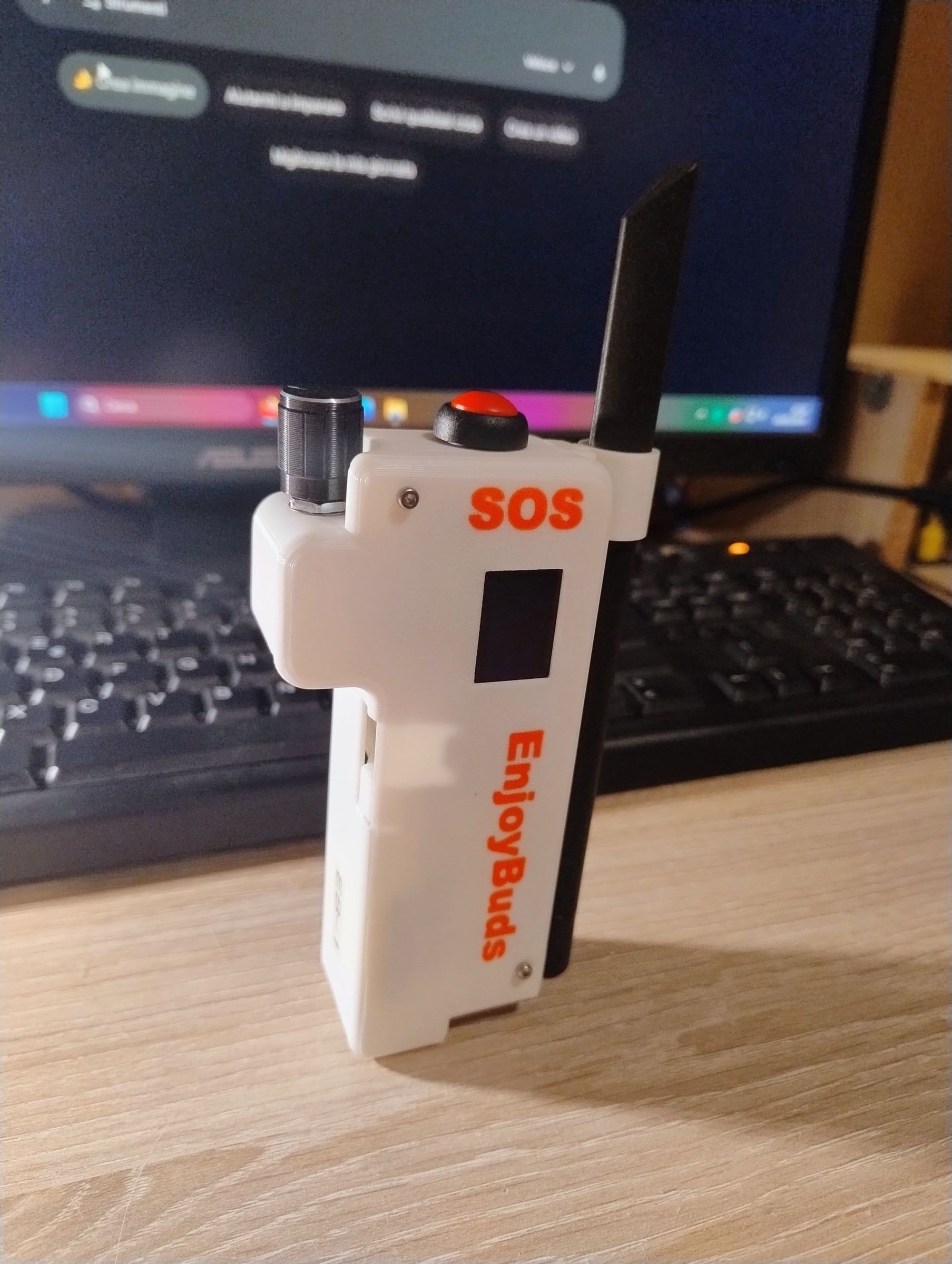 One of the first EnjoyBuds prototypes, white, with a red button and the word SOS