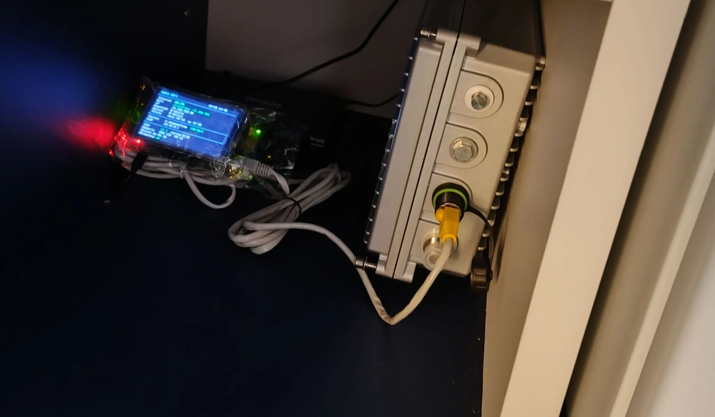 The Raspberry Pi with its small screen on and the network cables in a corner of the pantry, next to a grey box fixed to the wall