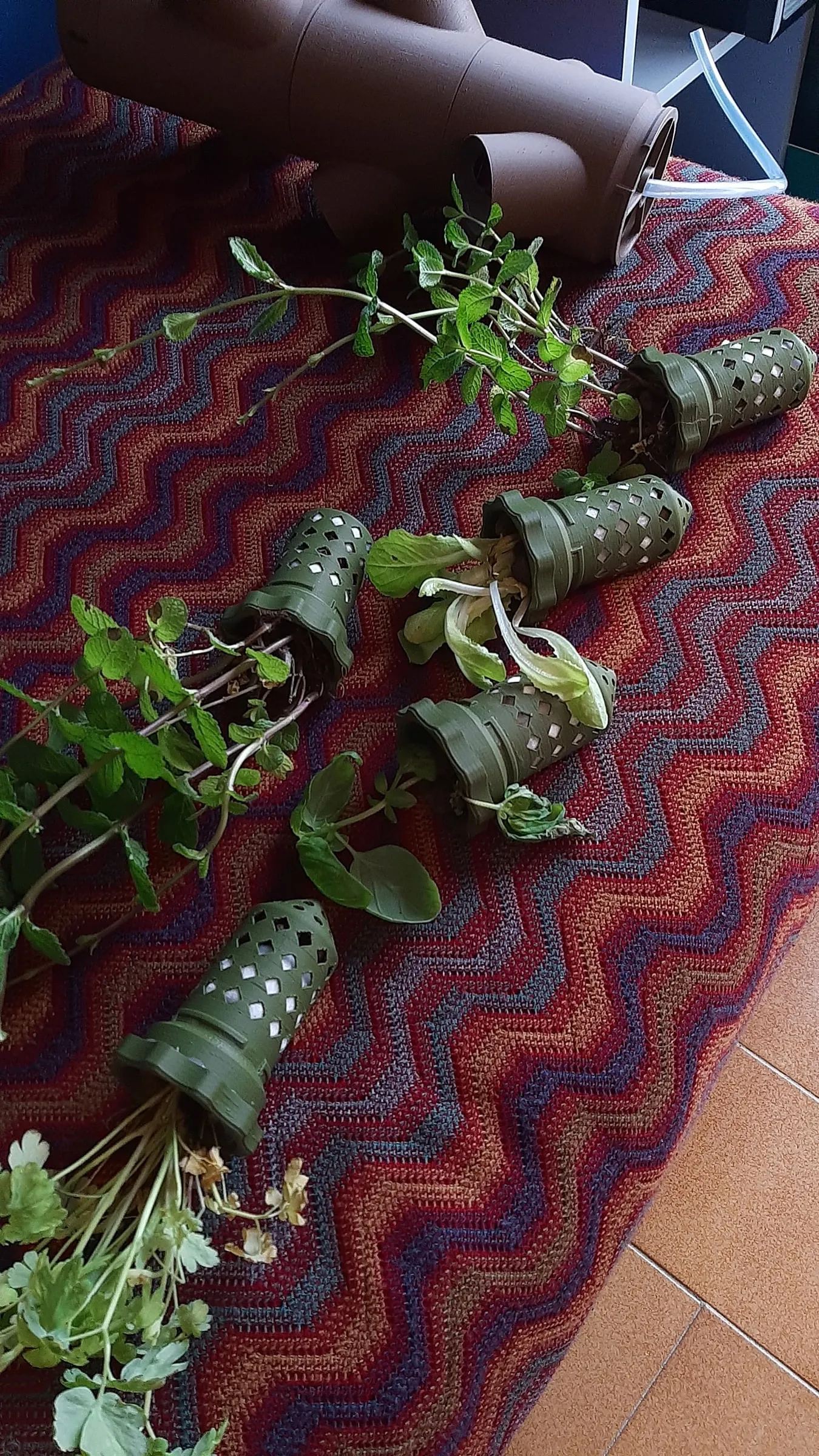 Some small plants with their roots in the green perforated pots, lying on a striped blanket next to a piece of the tower