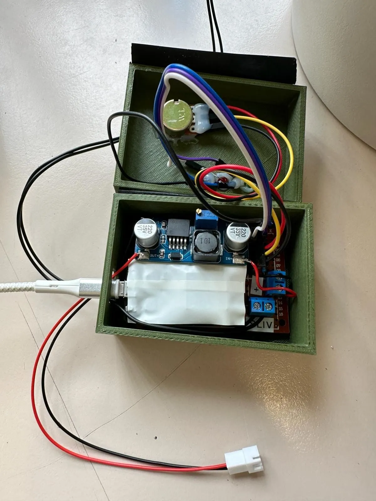 The inside of the green printed box: the potentiometer, a blue voltage converter, the relay board and coloured wires